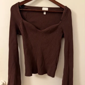 Brun ribbad tröja från H&M - Säljer en snygg brun ribbad tröja från H&M med en v-ringad design. Tröjan har långa ärmar och en figurnära passform som passar perfekt för höst och vinter. Perfekt för att hålla stilen när det blir kallare ute.