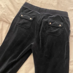 Mörkblå byxor från Juicy Couture - Snygga blå byxor från Juicy Couture i mjukt material. Byxorna har praktiska fickor med knappar baktill och snörning i midjan för en bekväm passform. Perfekta för en avslappnad stil.