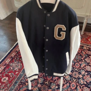 Blå och vit bomberjacka med bokstavsdetalj - Snygg bomberjacka i blått och vitt. Jackan har knappar framtill och ribbade muddar vid ärmslut och nederkant. Perfekt för en cool och avslappnad stil.