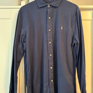 Blå långärmad skjorta från Polo Ralph Lauren - Snygg blå långärmad skjorta från Polo Ralph Lauren med klassisk krage och knappar framtill. Skjortan har en broderad logotyp på bröstet och är perfekt för en stilren look.