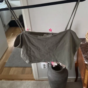 Olivgrön topp - Säljer en stilren olivgrön topp med smala axelband. Perfekt för varma sommardagar eller som ett lager under en jacka. Toppen har en enkel och elegant design.
