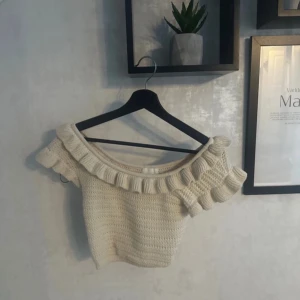 Beige stickad offshoulder topp från H&M - Säljer en söt beige stickad offshoulder topp från H&M. Toppen har volangdetaljer längs halsringningen och är perfekt för en stilren look. Passar bra till både jeans och kjol.