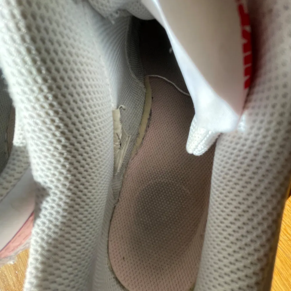 Säljer ett par vita Nike sneakers med rosa detaljer och snörning. Skorna har en klassisk design med perforeringar på tån för ventilation. Perfekta för en avslappnad stil.. Kengät.