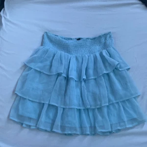 Ljusblå volangkjol från Vero Moda - Säljer en söt ljusblå volangkjol från Vero Moda. Kjolen har flera lager av volanger och en elastisk midja för bekväm passform. Perfekt för en somrig look!