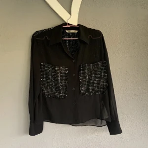 Svart transparent skjorta från Zara - Snygg svart transparent skjorta från Zara med långa ärmar och knappar framtill. Skjortan har två stora rutiga fickor i svart och vitt på bröstet och en matchande detalj på ryggen. Perfekt för en stilren look.