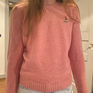 Rosa tröja från Polo Ralph Lauren - Säljer en snygg rosa tröja från Polo Ralph Lauren. Tröjan har en klassisk design med rund hals och långa ärmar. Den är dekorerad med det ikoniska Polo-logotypen på bröstet. Perfekt för en stilren look!