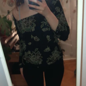 Svart blommig topp från Frazier Lawrence - Säljer en svart topp med blommigt mönster från Frazier Lawrence. Toppen har en offshoulder-design och trekvartsärmar, vilket ger en stilren och trendig look. Perfekt för att piffa upp garderoben med lite blommig charm!