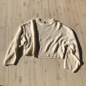 Vit stickad croppad tröja - Säljer en snygg beige ribbad tröja med croppad passform. Perfekt för en stilren look. Tröjan har långa ärmar och en rund halsringning. Passar utmärkt till både jeans och kjol.
