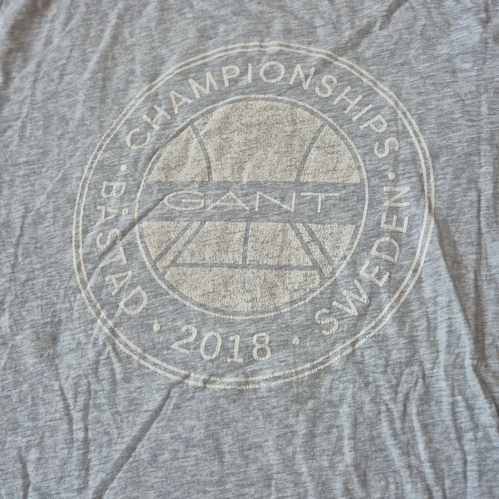 Säljer en grå t-shirt från Gant med tryck 'Championships Båstad Sweden 2018' på framsidan. T-shirten är kortärmad och har en rund halsringning. Perfekt för en avslappnad stil. Storleken är barn 176, 16 år. T-paidat.