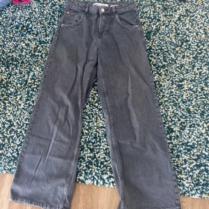 Grå jeans med vida ben - Säljer ett par grå jeans med vida ben och hög midja. De har en klassisk femficksdesign och är tillverkade i denim. Perfekta för en avslappnad stil. De är lite slitna nere vid fötterna.