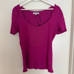 Rosa ribbad topp från Morgan - Säljer en snygg rosa ribbad topp från Morgan. Toppen har en v-ringad design och korta ärmar, perfekt för en stilren look. Den är tillverkad i ett mjukt material som ger en bekväm passform.