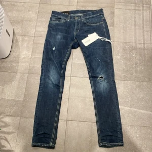 Mörkblå jeansbyxor - Snygga mörkblå jeans med slitna detaljer och en klassisk femficksdesign. Byxorna har en normal passform och är perfekta för en avslappnad stil. De har en dragkedja och knapp framtill.