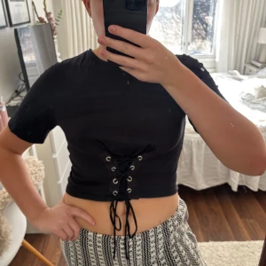 Svart croppad topp från Zara - Säljer en svart croppad topp från Zara med snörning framtill. Toppen har korta ärmar och en rund halsringning. Perfekt för en trendig look! 🖤