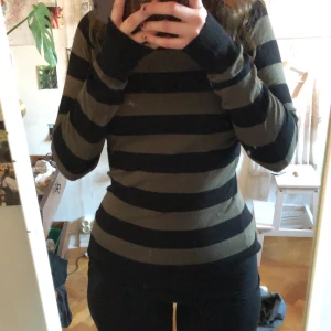 Randig tröja från French Connection - Säljer en randig tröja från French Connection i svart och olivgrön. Tröjan har långa ärmar och en normal passform, perfekt för höst och vinter. Den är tillverkad i ett mjukt material som känns skönt mot huden.