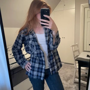 Blå flanellskjorta  - Säljer en blå rutig flanellskjorta, jättesnygg att ha öppen över en tröja. Tyvärr har en av knapparna på ena ärmen gått av men annars är den i bra skick💙