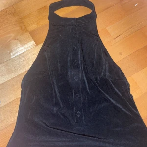 Svart topp från Kookai - Snygg svart klänning från Kookai med halterneck-design och knappar framtill. Perfekt för en elegant kvällslook.