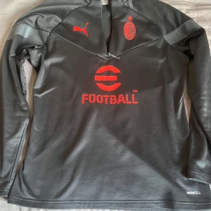 AC Milan halfzip - Säljer en svart långärmad tröja från Puma med AC Milan-logga på framsidan. Half zip träningströja som är perfekt för att köra fotboll med på en lite kylig sommarkväll, har använts endast ett fåtal gånger.
