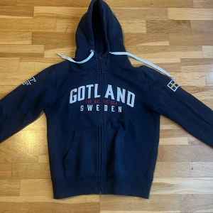 Mörkblå hoodie med Gotland-tryck - Säljer en mörkblå hoodie med dragkedja och Gotland-tryck på framsidan. Tröjan har en justerbar huva med vita snören( obs ringarna på snörena är en gång lagade , men egen bedömning ) . Perfekt på svalare sommarkvällar eller annat. Hör bara av er om frågor eller annat☀️🇸🇪🌸