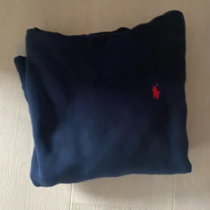 Mörkblå hoodie från Ralph Lauren Xs - Säljer en snygg mörkblå hoodie från Ralph Lauren med det klassiska röda logotypen på bröstet. Tröjan har en praktisk känguruficka och justerbar huva med vita snören. Perfekt för en avslappnad stil.