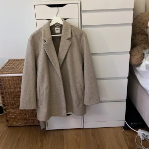 Beige kappa från ONLY - Säljer en stilren beige kappa från ONLY. Den har en klassisk design med knytband i midjan och långa ärmar. Perfekt för höst och vår. Kappan är tillverkad i ett mjukt material som ger en elegant look.
