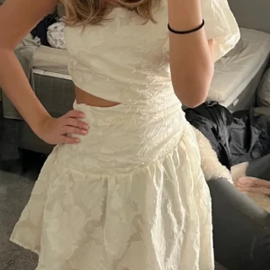 Vit blommig klänning - Charmig vit klänning med blommigt mönster, passar perfekt till studenten, tyvärr en reva under armhålan, men går enkelt att laga!