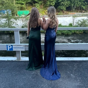 Marinblå långklänning med slits - Snygg blå långklänning i satin med smala axelband och en slits framtill. Bara använd en gång (9:ans bal) och vet inte vid vilket mer tillfälle den kan komma till användning! Nypris är 1300kr, bara använd 1 gång och är i jätte fint skick! Finns även matchande klackskor till i storlek 38 om man skulle vara intresserad💕