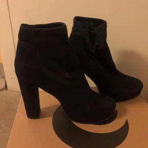 Svarta boots från Tiamo - Snygga svarta boots från Tiamo med hög klack och rund tå. Skorna har en stilren design och är perfekta för att lyfta din outfit. Tillverkade i syntetmaterial med en robust sula för extra grepp.