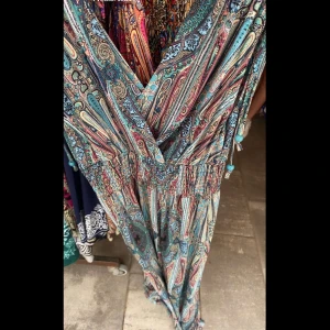 Mönstrad långklänning - Snygg långklänning med ett färgglatt paisleymönster i blått, rött och beige. Klänningen har en omlott-design och knytband vid axlarna för en justerbar passform. Perfekt för sommarens alla tillfällen! Den är one size! Har ingen bild på och kan inte ta då den är inte här hos mig!