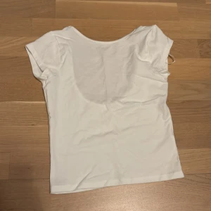 Vit kortärmad topp från Gina Tricot - Säljer en stilren vit topp från Gina Tricot. Den har korta ärmar och en djup rundad halsringning. Perfekt för en enkel och fräsch look. Passar bra till både jeans och kjol.