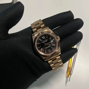 Guldfärgad klocka med svart urtavla - Elegant guldfärgad klocka med svart urtavla och datumvisning. Klockan har en klassisk design med en robust länkarmband och tydliga markeringar på urtavlan. Perfekt för den som söker en stilren accessoar.
