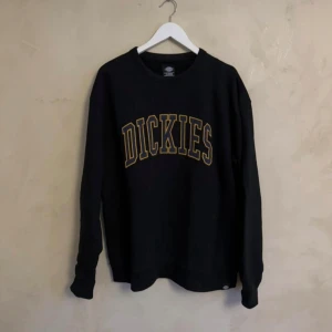 Svart sweatshirt från Dickies - Säljer en svart tröja från Dickies med deras logga i gult på bröstet. Tröjan har långa ärmar och en rund halsringning. Perfekt för en avslappnad stil.