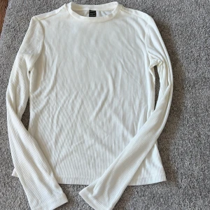 Vit ribbad långärmad topp från evolusHEIN - Säljer en stilren vit ribbad topp från evolusHEIN. Den har en klassisk design med långa ärmar och en bekväm passform. Perfekt för lager-på-lager eller att bära som den är. Storlek S. Använd fåtal gånger. 