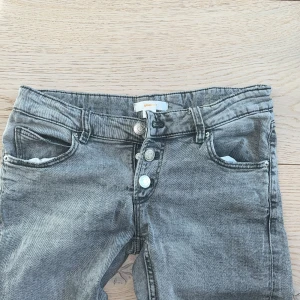 Grå jeans med knappar - Snygga grå jeans med en cool tvätt och knappar framtill. De har en klassisk femficksdesign och raka ben. Perfekta för en avslappnad stil.
