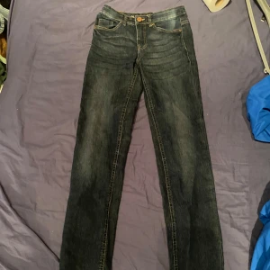 Mörkblå jeansbyxor - Säljer ett par mörkblå jeansbyxor med normal passform och hög midja. Byxorna har klassisk femficksdesign och stängs med en knapp och dragkedja. Perfekta för en avslappnad stil. Dom är lite utsvängda vid slutet av benen typ som bootcut.