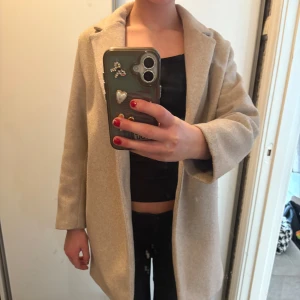 Beige kappa - Snygg beige kappa med klassisk design och normal passform. Perfekt för höst och vår. Kappan har långa ärmar och en stilren look som passar till många olika outfits.