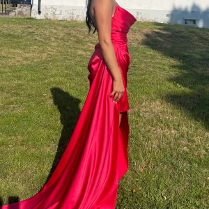 Fest/balklänning  - Säljer en fantastisk röd axelbandslös långklänning med slits. Perfekt för en elegant kväll. Klänningen har en vacker drapering och en lång svepande kjol. Pris kan diskuteras vid snabb affär.