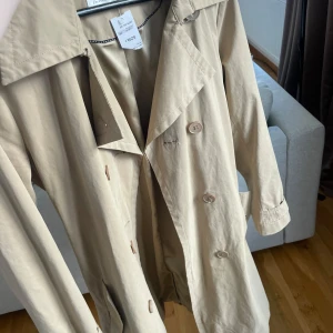 Beige trenchcoat från InWear - Snygg beige trenchcoat från InWear. Jackan har långa ärmar och knappar framtill samt ett bälte i midjan. Perfekt för vår och höst! Storlek 40 men passar allt från 34-40. Köpt på second hand för 529kr och är k nyskick. 