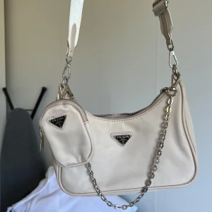 Beige axelväska  - Snygg beige axelväska med en matchande liten väska. Väskan har en justerbar axelrem och en kedjedetalj. Perfekt för att bära dina nödvändigheter med stil. Endast haft i garderob 