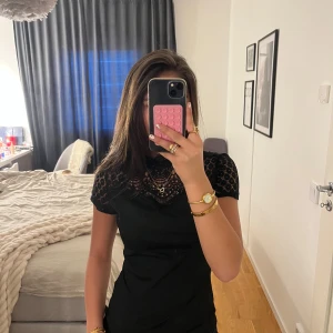 Svart ribbad topp med spetsdetaljer - Snygg svart ribbad topp med spetsdetaljer på axlarna och runt halsen. Toppen har en tight passform och korta ärmar. Perfekt för en stilren look.✨🥰