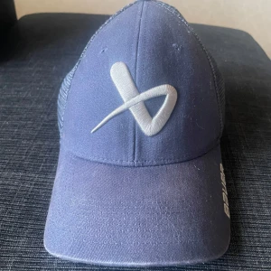 Blå keps från Bauer - Snygg blå keps från Bauer med ett stilrent broderat märke framtill. Kepsen har en mesh-design baktill för extra ventilation och en justerbar rem för perfekt passform. Perfekt för en sportig look! Färgen återspeglas lite dåligt på bilden, kepsen är väldigt mörkblå och i fint skick. 