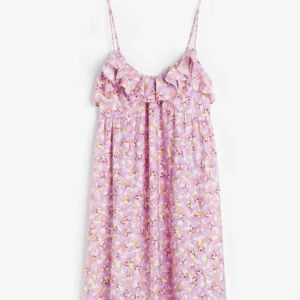 Lila blommig klänning med volangdetalj - Charmig lila klänning med blommigt mönster och volangdetalj vid bysten. Axelbandslös design med smala axelband, perfekt för sommarens varma dagar. Klänningen är använd endast en gång. (Andra bilden är lånad)