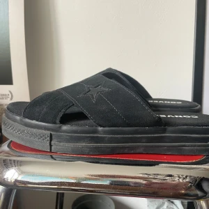 Svarta sandaler från Converse - Snygga svarta sandaler från Converse med korsade remmar och en stjärndetalj. Remmarna är i mocka, därav grusdamm-fläckar som lätt går att borsta bort. :)  Skorna är bara använda av ett fåtal gånger men de är väldigt bekväma att gå i med en tjock sula. Skorna är storlek 40 men passar mig som har 39.