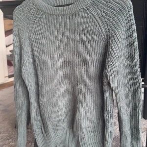 Turkos stickad tröja från The Black Label Collection - Säljer en stilren grå stickad tröja från The Black Label Collection. Tröjan har en klassisk rund hals och långa ärmar, perfekt för kyligare dagar. Den ribbade strukturen ger en snygg och tidlös look. Passar utmärkt till både jeans och chinos.
