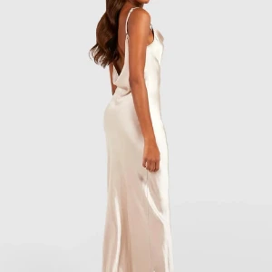 Champagnefärgad långklänning - Elegant champagnefärgad långklänning i satin med smala axelband och öppen rygg. Perfekt för en glamorös kväll med sin slanka passform och mjuka glans.