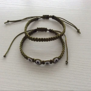 Baba armband set  - Olivgröna armband set BABA Två handgjorda armband i olivgrönt snöre med justerbar knut. Ett av armbanden har vita bokstavspärlor som bildar ordet 'BABA'. Perfekt för en personlig touch eller som en gåva.