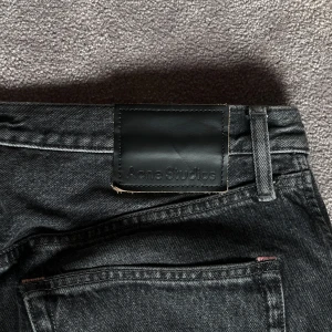 Svarta jeans från Acne Studios - Snygga svarta jeans från Acne Studios med klassisk femficksdesign. De har en rak passform och är tillverkade i ett slitstarkt denimtyg. Perfekta för en stilren look. W30 L34. En liten fläck förekommer på främre benet men syns knappt, går nog bort om man tar npgit söags medel på. 