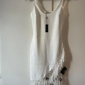 Vit klänning med fransdetaljer - Snygg vit klänning från NLY One med fransdetaljer längs nederkanten.           Aldrig använt, helt ny med prislapp kvar.  Storlek S