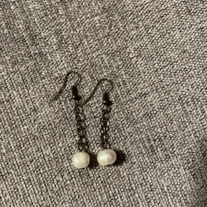 Örhängen med äkta pärlor från Hawaii - Säljer ett par eleganta handgjorda örhängen som jag köpte i Hawaii. De har en mörk kedja som ger en fin kontrast till pärlorna. Perfekta för att ge en stilren touch till din outfit. Aldrig använda. 