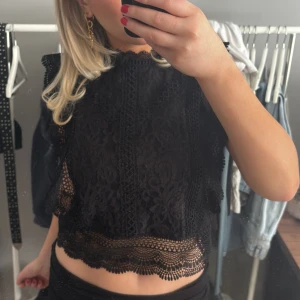 Svart spetsblus - Säljer en elegant svart spetsblus med vackra detaljer. Blusen är ärmlös och har en fin spetsdesign som ger en romantisk känsla. Perfekt för att klä upp vilken outfit som helst.
