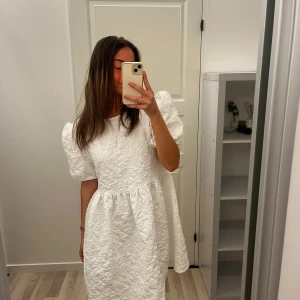 Vit klänning med puffärmar - Säljer en elegant vit klänning med puffiga kortärmar och en texturerad yta. Perfekt för studenten. Den är oanvänd. Nypris 745